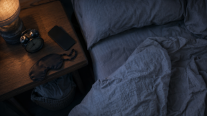 An alarm clock beside a rumpled bed representing repeated snoozing and sleep inertia