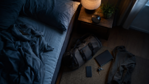 A packed travel bag beside a restless bed representing stress-related early waking